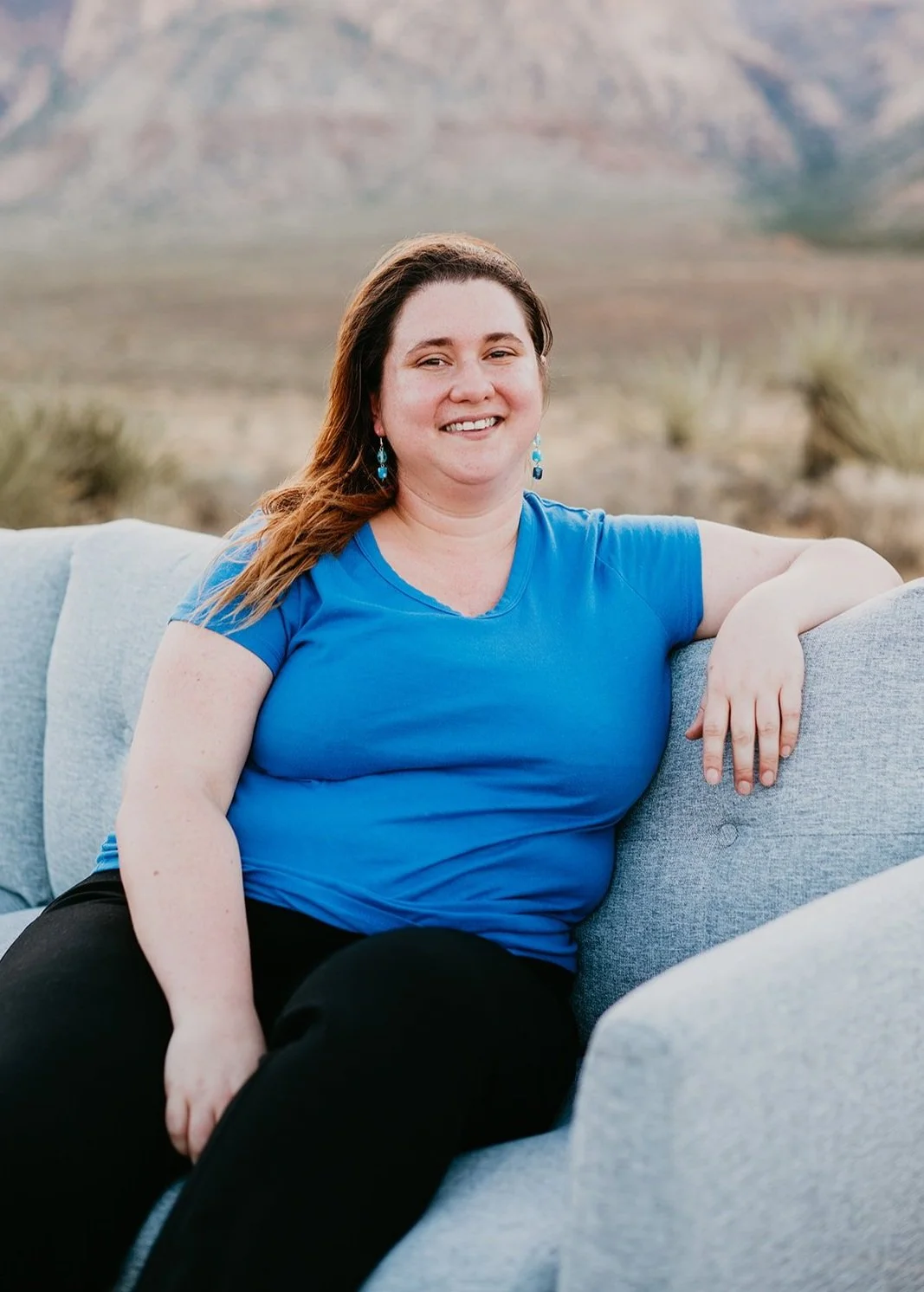 Person sitting on a gray couch outdoors, wearing a blue shirt and black pants, with a desert landscape in the background.